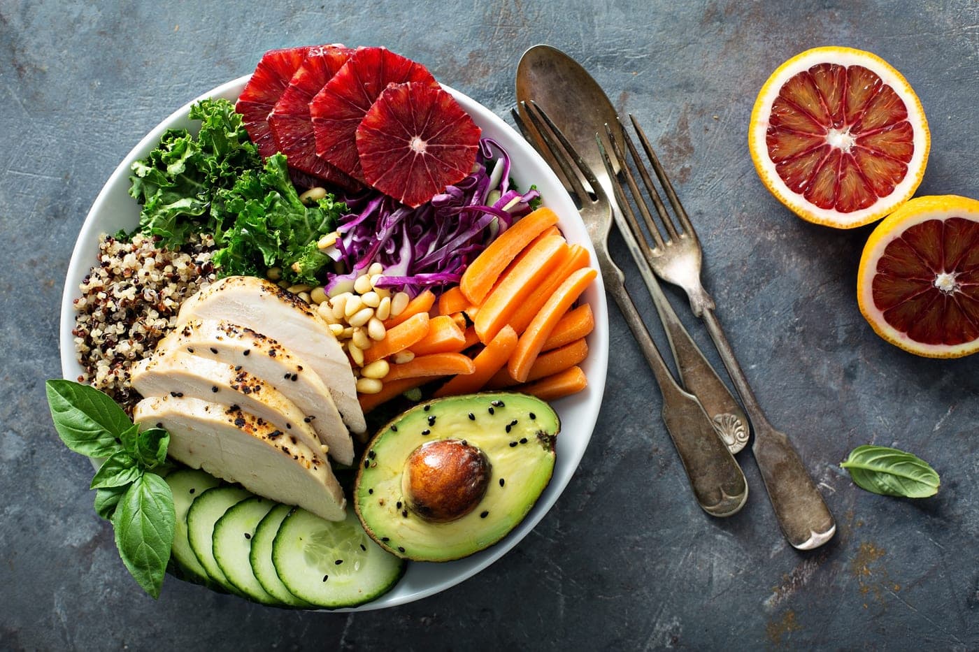 A colorful, nutrient-rich bowl with grilled chicken, avocado, kale, and blood orange